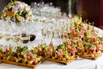 the buffet at the reception. Glasses of wine and champagne. Assortment of canapes on wooden board....