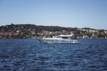 Unrecognizable people ride luxury white yacht on Bosphorus in a sunny summer day in Istanbul. European side is in the background.