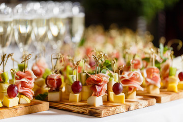 the buffet at the reception. Glasses of wine and champagne. Assortment of canapes on wooden board. Banquet service. catering food, snacks with cheese, jamon, prosciutto and fruit - 225240994