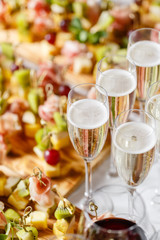 the buffet at the reception. Glasses of wine and champagne. Assortment of canapes on wooden board. Banquet service. catering food, snacks with cheese, jamon, prosciutto and fruit