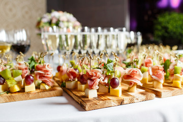 the buffet at the reception. Glasses of wine and champagne. Assortment of canapes on wooden board. Banquet service. catering food, snacks with cheese, jamon, prosciutto and fruit - obrazy, fototapety, plakaty