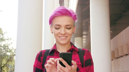 A young woman with a pink short hair using a phone in the city street. Close-up shot. Soft focus. Dolly shot. Lens flare