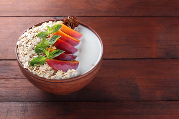 Oatmeal with fruits and green mint. Oat flakes with milk on wooden background. Healthy food. Breakfast for vegan. Dry oats with peaches, anise and milk. Copy space