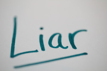 The word Liar written in green marker on white paper. Top and bottom purposefully out of focus for effect.