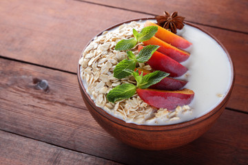 Oatmeal with fruits and green mint. Oat flakes with milk on wooden background. Healthy food. Breakfast for vegan. Dry oats with peaches, anise and milk. Copy space