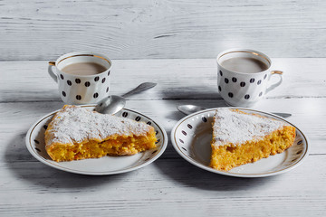 Pieces of fragrant pumpkin pie on a wooden table with cups of coffee