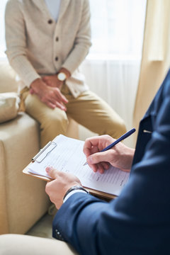 Closeup of unrecognizable psychiatrist holding clipboard and taking noted while consulting patient, copy space