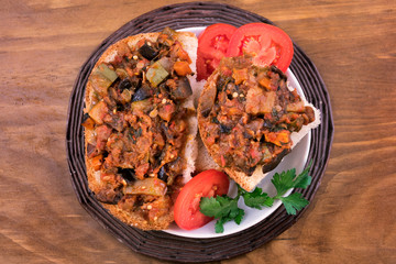 A portion of vegetable stew on pieces of white bread, decorated with slices of tomatoes and parsley leaves.