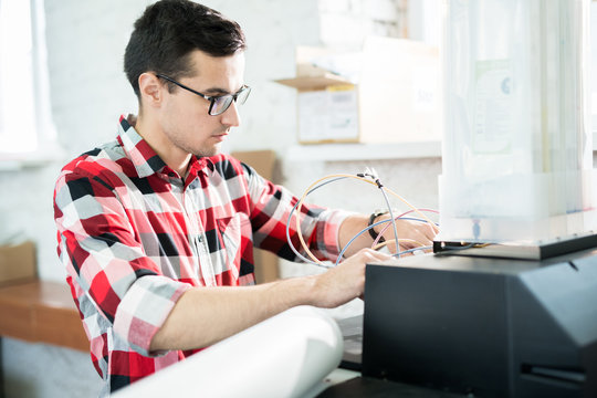 Serious Busy Handsome Young Male Engineer In Glasses Repairing Printer In Office Of Printing Company And Checking Ink Cables