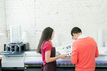 Rear view of busy printing specialists examining banner with text and standing at large format...