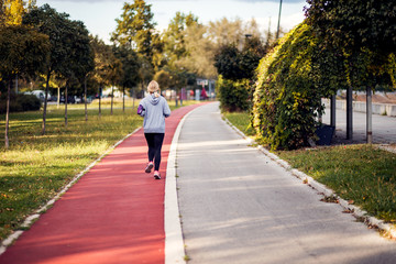 Fototapeta premium Rear view at female runner running on racetrack in a park