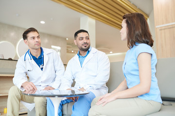 Fototapeta premium Portrait of two doctors listening to female patient during medical examination in modern clinic, copy space