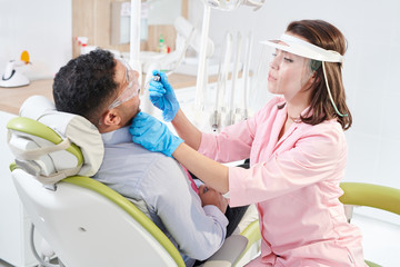 Side view portrait of young female dentist wearing face mask working with patient sitting in dental chair during teeth treatment, copy space