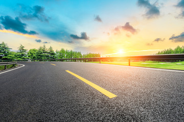 Naklejka premium Empty asphalt road and green forest with colorful clouds at sunset