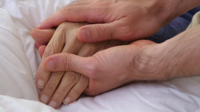 Close-up of a young man holding his grandparent's hand. Filmed in 4K