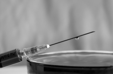 Black and white syringe with a drop on the needle
