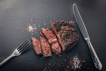 Sliced beef steak sous-vide sliced on slate board with cutlery