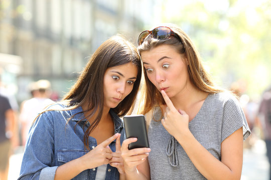 Perplexed girls checking smart phone outdoors