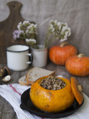 Traditional buckwheat porridge with meat and vegetables baked in pumpkin. Autumn dish, pumpkin, autumn bouquet of flowers, white mug on an old wooden background. Selective focus, copy space