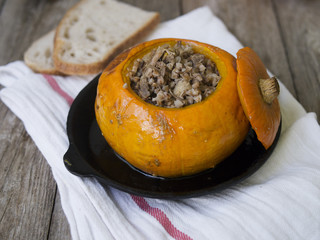 Traditional buckwheat porridge with meat and vegetables baked in pumpkin on wooden background. Autumn dish. Selective focus, copy space
