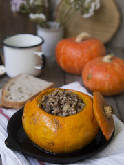 Traditional buckwheat porridge with meat and vegetables baked in pumpkin. Autumn dish, pumpkin, autumn bouquet of flowers, white mug on an old wooden background. Selective focus, copy space