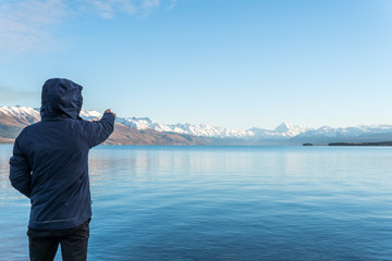 Man wearing blue Jacket and pointing at Mount Cook, New Zealand