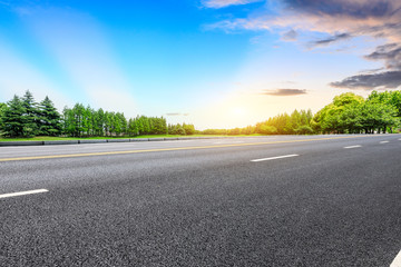 Empty asphalt road and green forest with colorful clouds at sunset