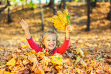 Happy little girl plays with autumn leaves in the park