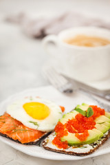 Avocado and red caviar, smoked salmon and fried egg rye toasts for breakfast, close up