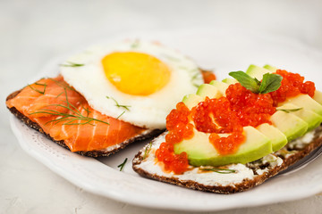 Avocado and red caviar, smoked salmon and fried egg rye toasts for breakfast, close up