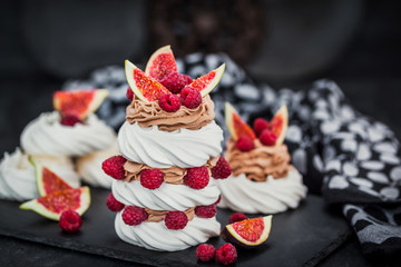 Delicious Pavlova meringue cakes decorated with chocolate cream, fresh figs and raspberries on dark background