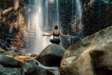 Woman meditating in front of a waterfall at Kionsom Park, Sabah, Malaysia.