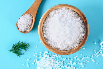 Fototapeta na wymiar Crystals of large sea salt in a wooden bowl and spoon and dill on a blue table.