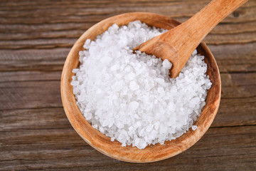 Crystals of large sea salt in a wooden bowl and spoon on a table.
