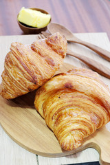 Croissant with butter on a wooden background.