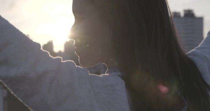 close up of Beautiful woman on a rooftop opening her arms into the golden sunrise 