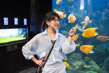 Young woman pointing fish in a tank with his finger at the aquarium.