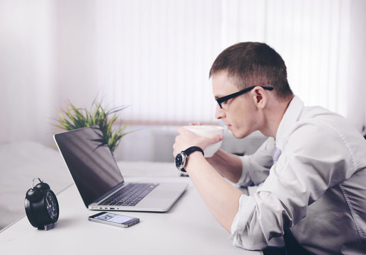 Young businessman trader sits at a table in the morning in a room near a laptop with a Cup of coffee.