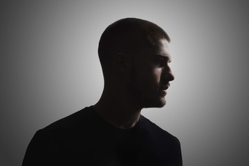 one young man, 20-25 years, moody dark portrait, profile. studio shot, gray background. head and...
