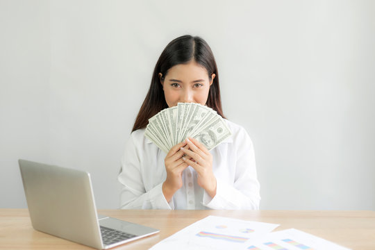 Successful beautiful Asian business young woman holding money US dollar bills in hand on office desk, business concept