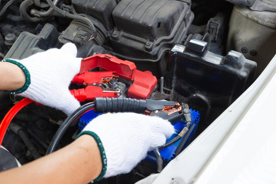Hands of Automotive Technician using jumper cables to charging vehicle battery and get car running again