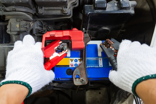 Hands of Automotive Technician using jumper cables to charging vehicle battery and get car running again