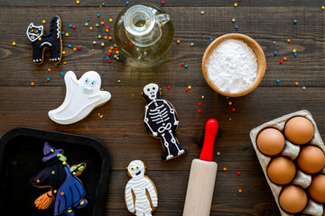 Make halloween gingerbread concept. Icing cookies near rolling pin, baking sheet, eggs, flour on dark wooden background top view