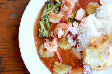 stir fried shrimp and Broccoli in thai red curry paste sauce with rice, Curry fried shrimps and cooked rice in white dish closeup on wooden table. Thai style food.