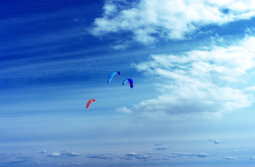 Colorful kites flying in a blue sky with air clouds. Kite surfing on the sea.