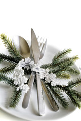 Picture of Christmastime table setting, white festive plate with knife and fork, shiny silver decoration, candle light, home interior, beautiful holiday dinnerware, romantic New Year dinner
