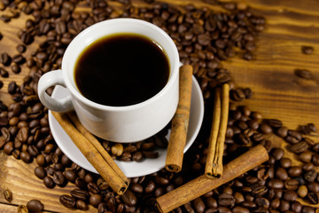 Cup of coffee, roasted coffee beans and cinnamon sticks on wooden table