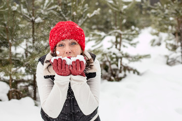 Portrait of girl in a red cap and warm jacket in the forest who have fun with snow