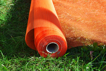 Building accesories - orange mesh roll for reinforcing walls in process of building insulation outdoors on green grass background.