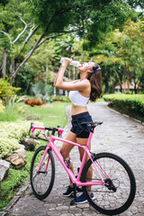 Naklejka premium Sport woman drinking water after riding a bicycle in the park.